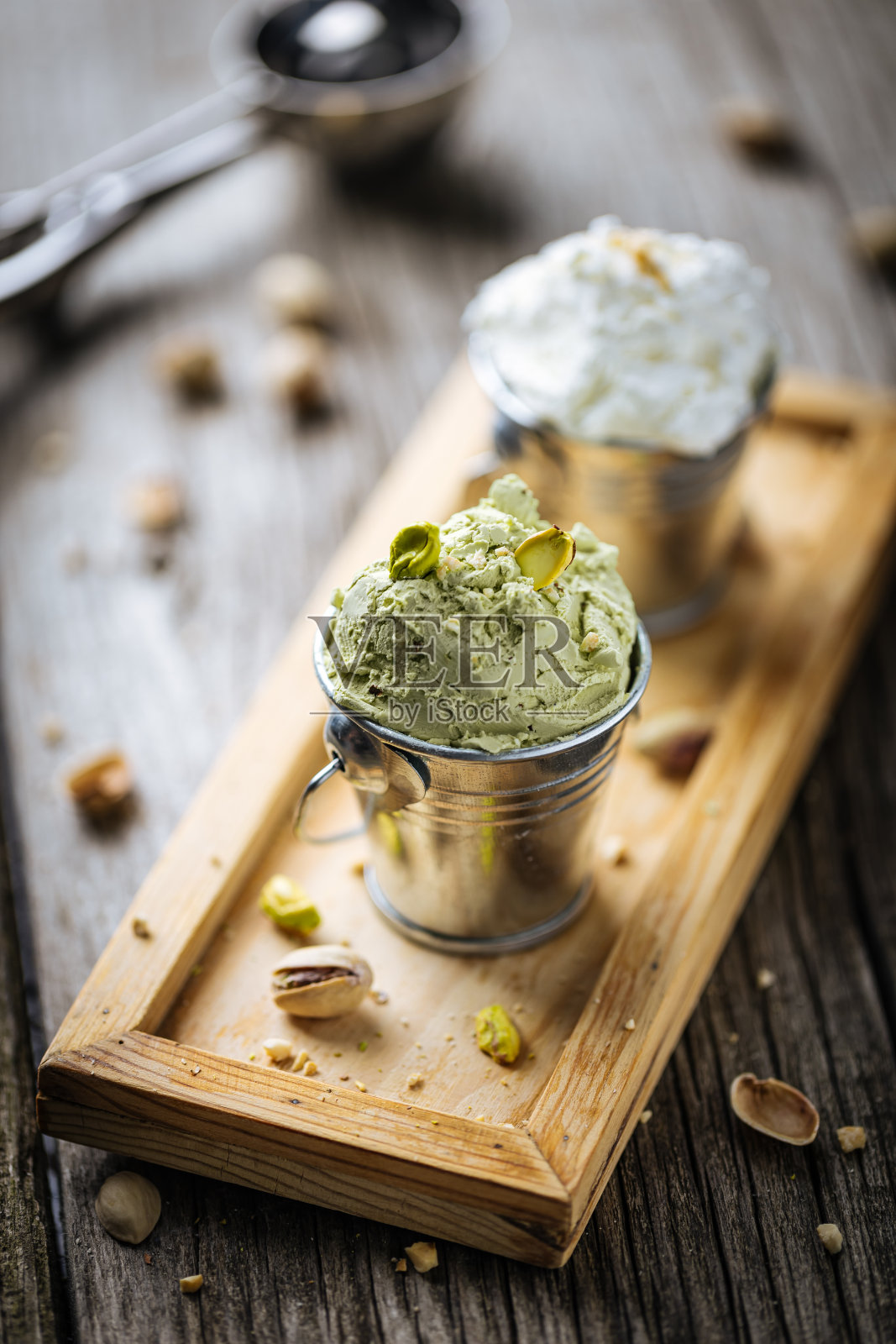 金属杯装开心果和香草冰淇淋球。装在木制托盘上，配上整个坚果。质朴的桌子上放着意大利冰淇淋。照片摄影图片