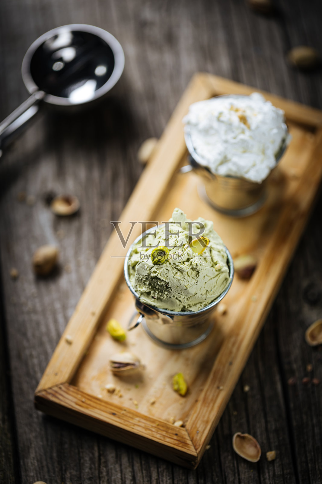 金属杯装开心果和香草冰淇淋球。装在木制托盘上，配上整个坚果。质朴的桌子上放着意大利冰淇淋。照片摄影图片