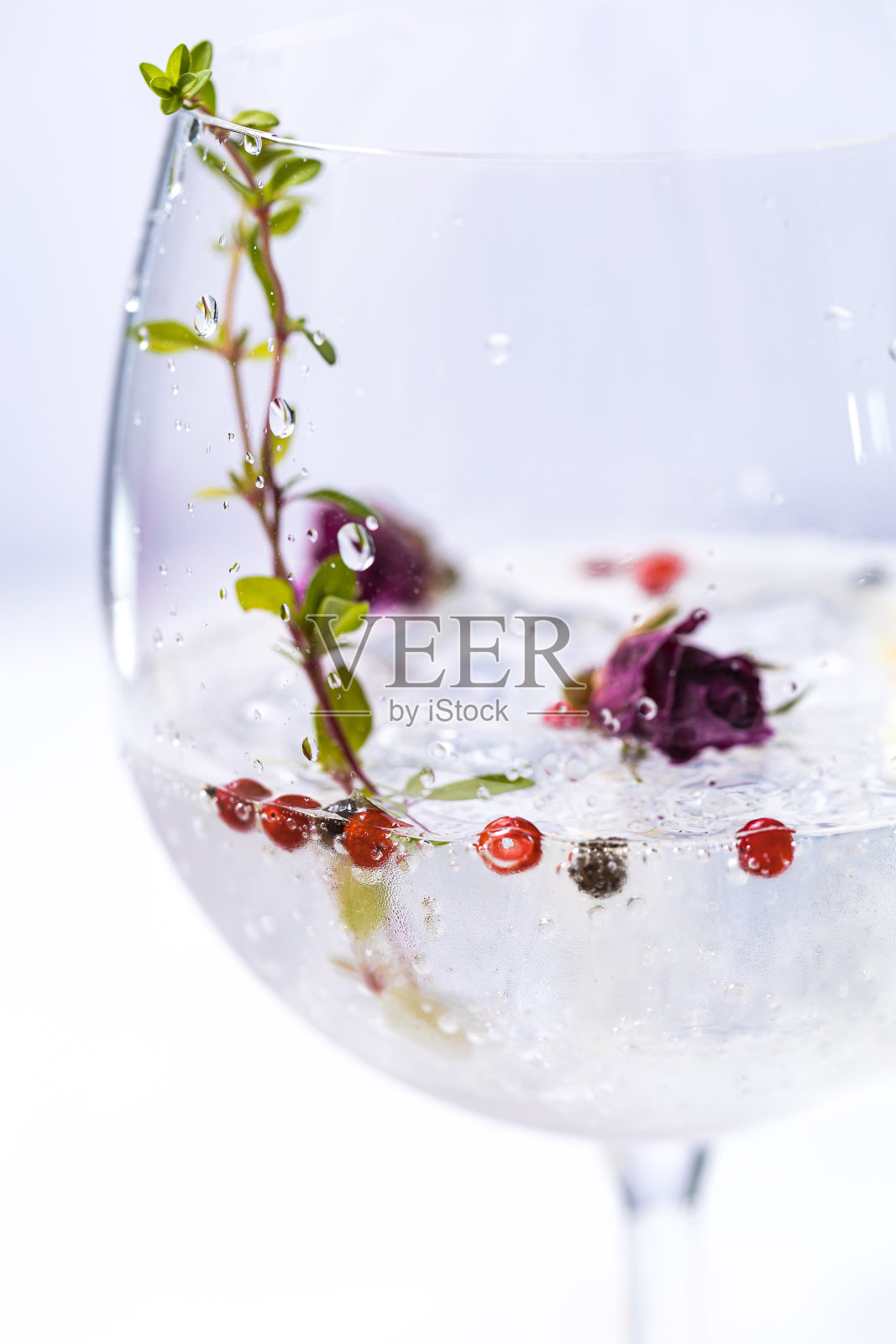 在白色明亮的环境中，在金酒杯中加入红辣椒、柠檬和玫瑰花蕾的杜松子酒汤力鸡尾酒。完美的夏日鸡尾酒。照片摄影图片