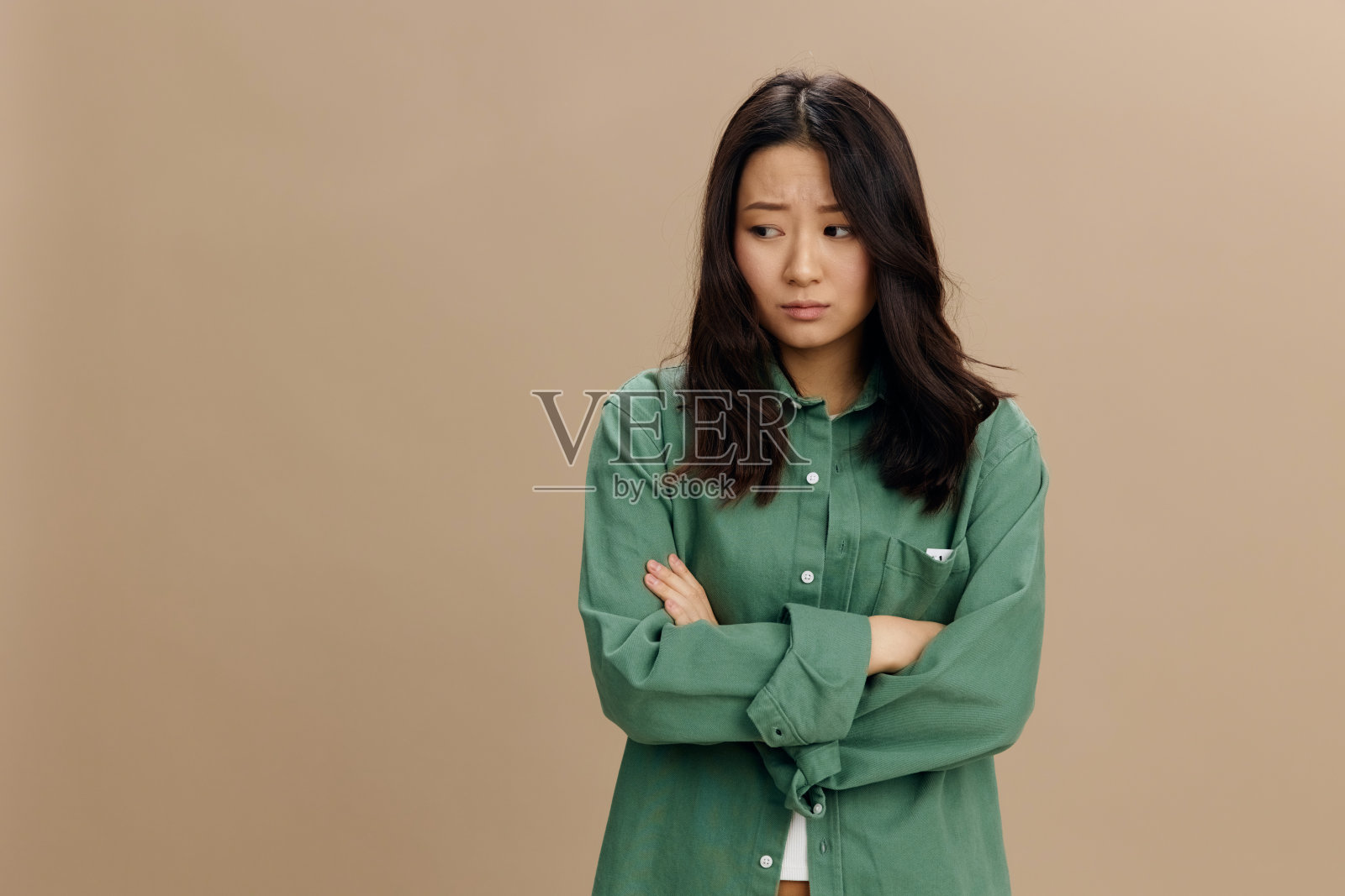 沮丧沮丧的亚洲学生年轻女子穿着卡其绿衬衫交叉双手在米色柔和的工作室背景上独自摆姿势。很酷的时尚报价。生活方式和情感概念照片摄影图片