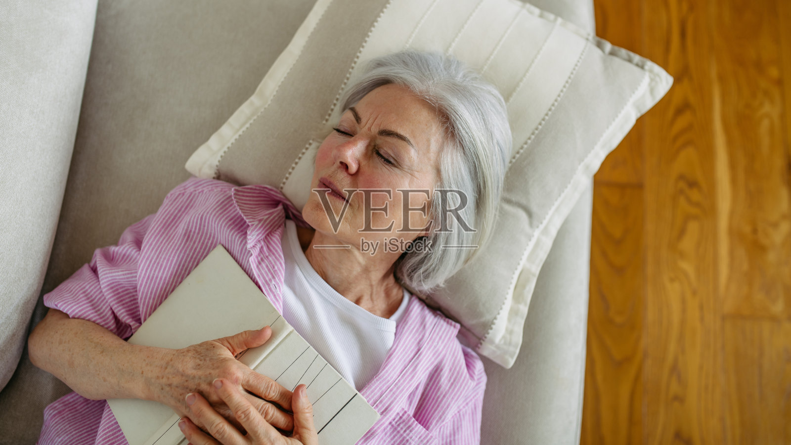 美丽成熟女人抱着书睡觉的俯视图。适合老年妇女的周末活动，在家放松。照片摄影图片