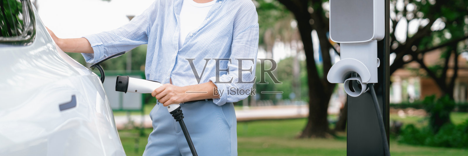 年轻女子在电动汽车充电站给电动汽车充电。高举照片摄影图片