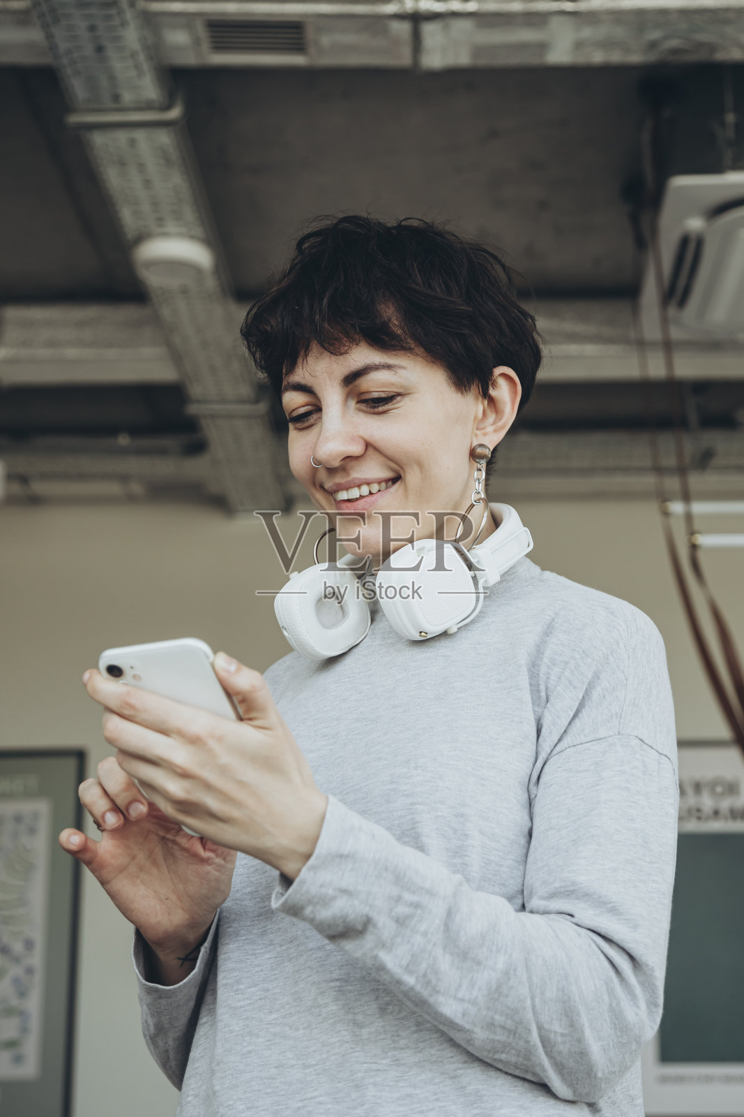 一头短发，戴着白色耳机的时尚女子正在使用智能手机。照片摄影图片