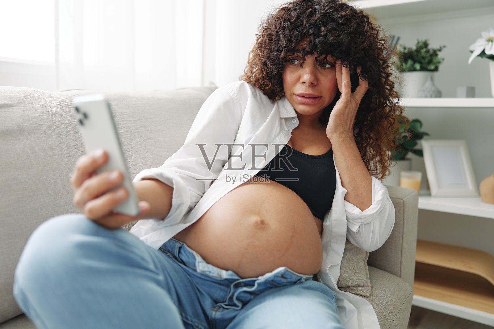 孕妇博主坐在家里的沙发上，用手机给自己拍照，自拍和视频通话，在线咨询医生，孕期管理，自由职业照片摄影图片