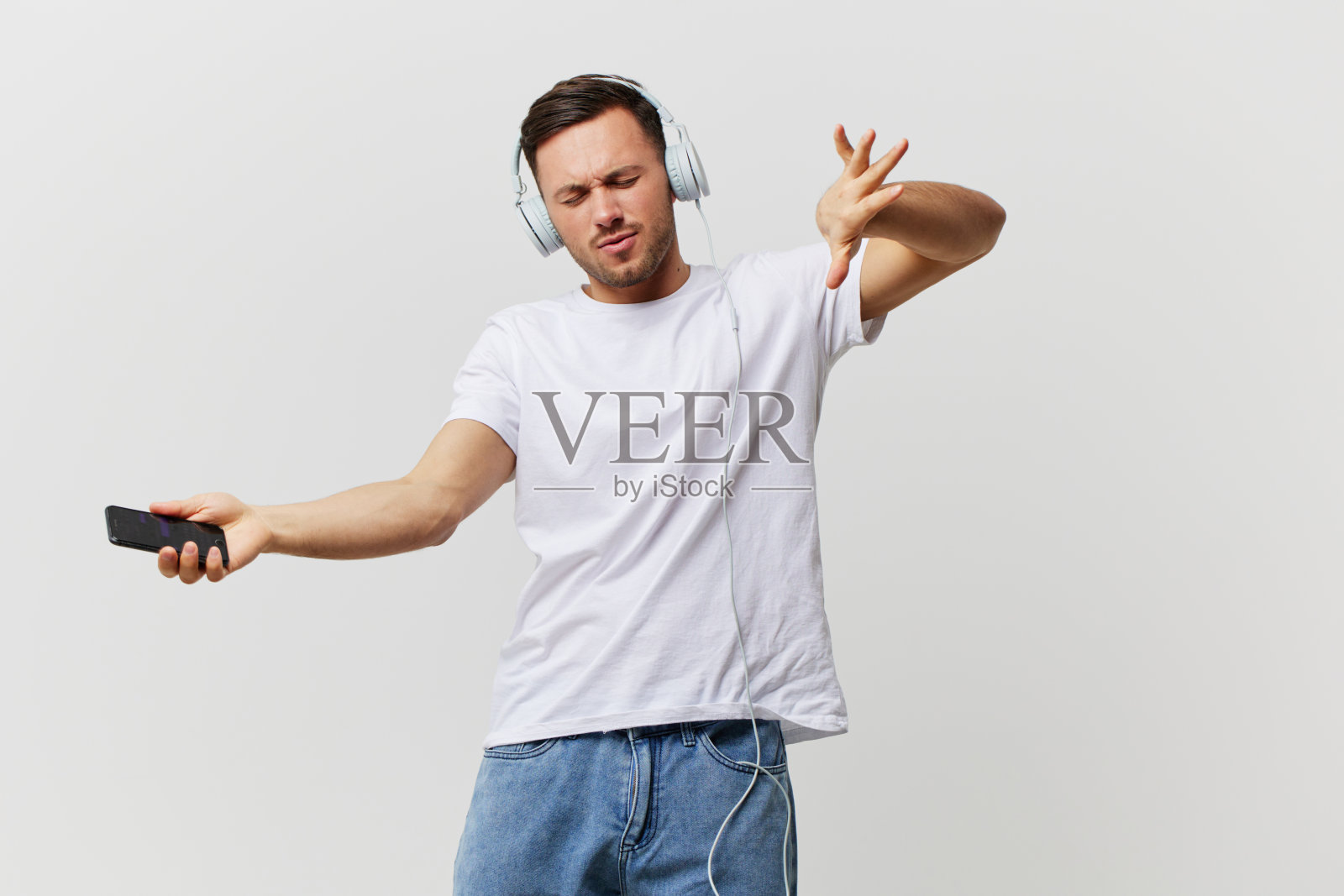 快乐迷人的晒黑英俊的男人穿着基本的t恤耳机听好的播放列表跳舞唱最喜欢的歌在白色的工作室背景上摆姿势。复制空间横幅模型。音乐的概念照片摄影图片