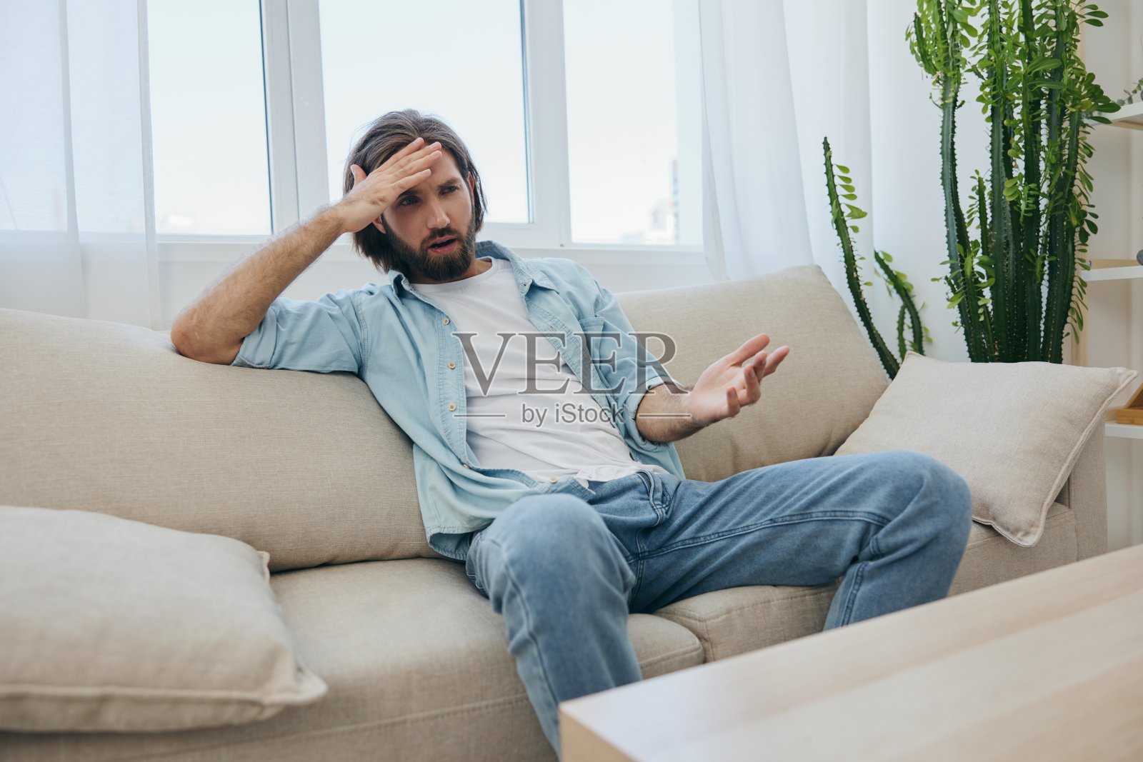 一位年轻的男性自由职业者在完成一项繁重的工作后，坐在沙发上，悲伤地倚在沙发上休息。照片摄影图片