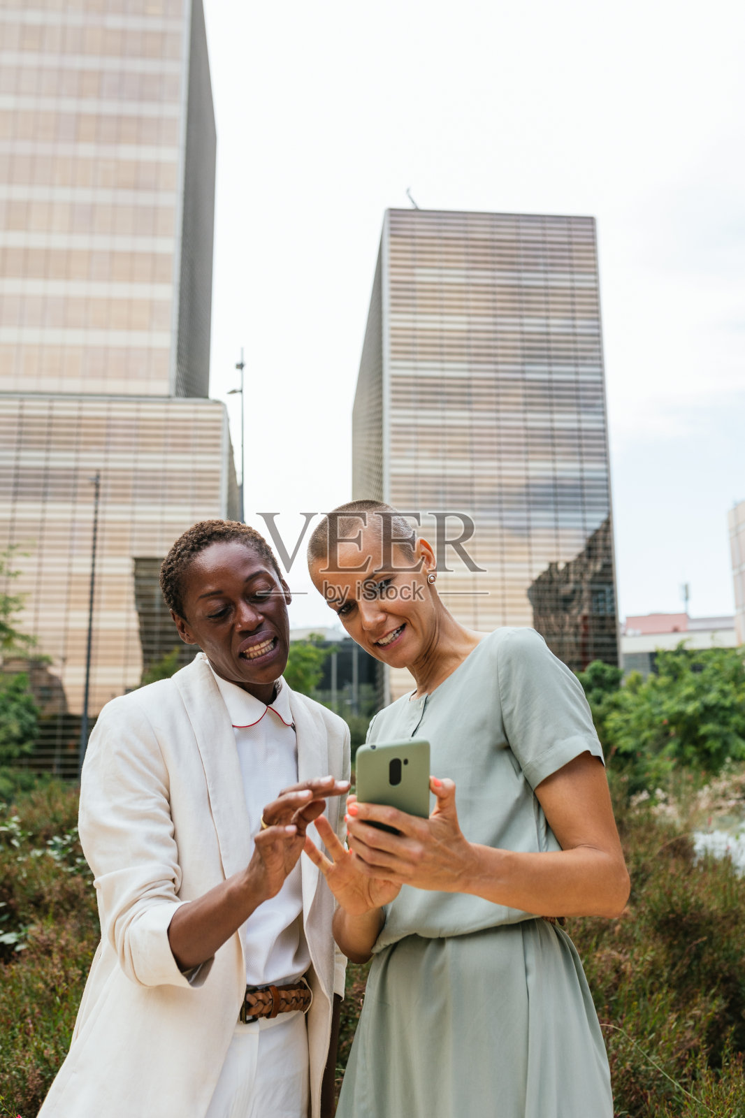 两个女人在城市里用智能手机分享欢笑照片摄影图片