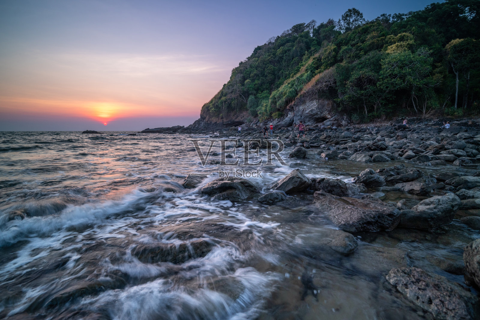 一个风景如画的灯塔守卫在悬崖上，海浪轻轻地抚摸着黄昏的岩石海岸。照片摄影图片