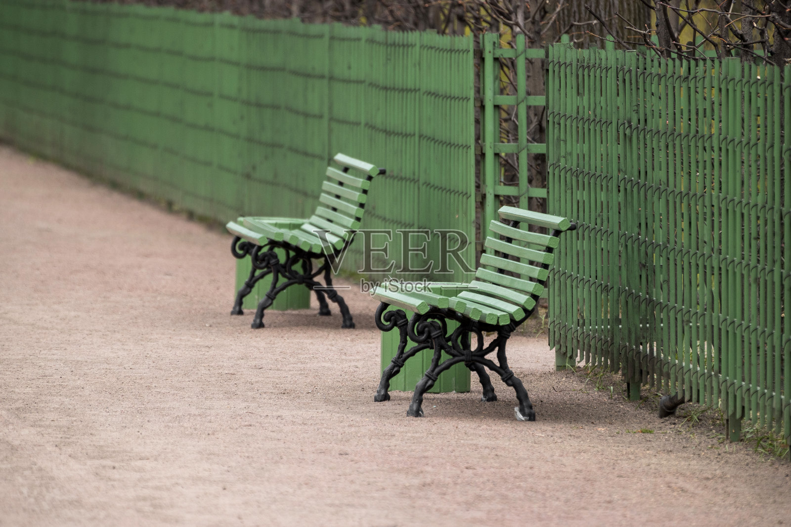 两条绿色的长凳沿着一条靠近绿色栅栏的人行道。照片摄影图片