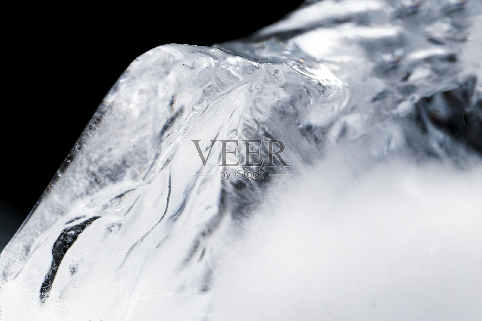 晶莹剔透的霜冻纹理的自然冰块在冷浅蓝色的色调，孤立的黑色背景。照片摄影图片