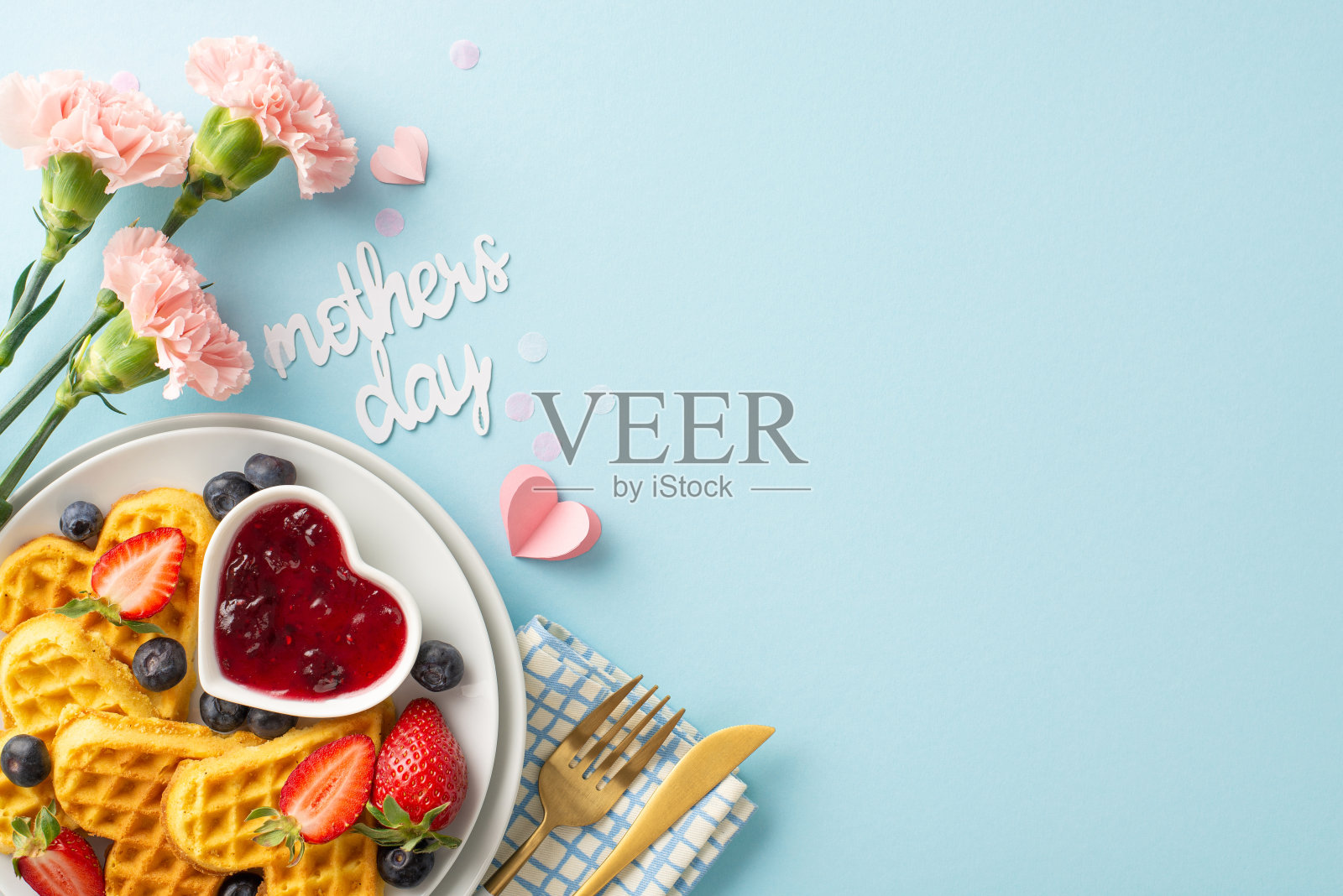 母亲节早餐:俯视图心形华夫饼，草莓，黑莓，果酱，叉子和勺子，餐巾，鲜花，问候“母亲节”，在一个柔软的蓝色背景，文字的空间照片摄影图片