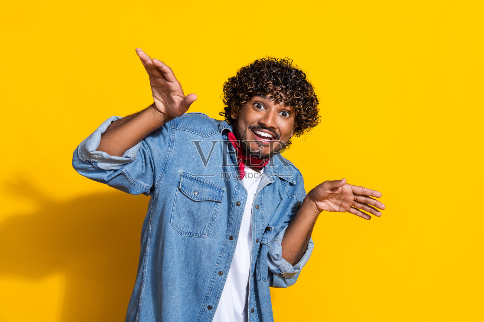 照片肖像迷人的年轻人双手飞扬俏皮穿着时髦的牛仔服装红色围巾孤立在黄色的背景照片摄影图片