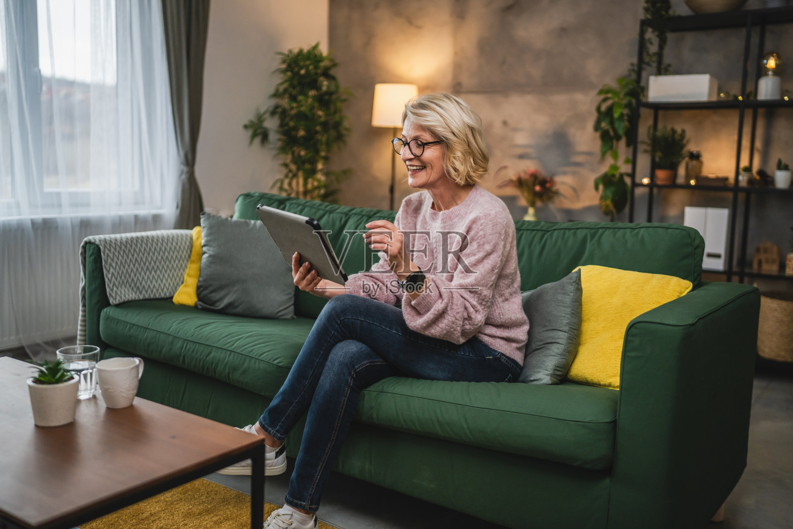 戴眼镜的成熟金发女人在家里使用数码平板电脑照片摄影图片