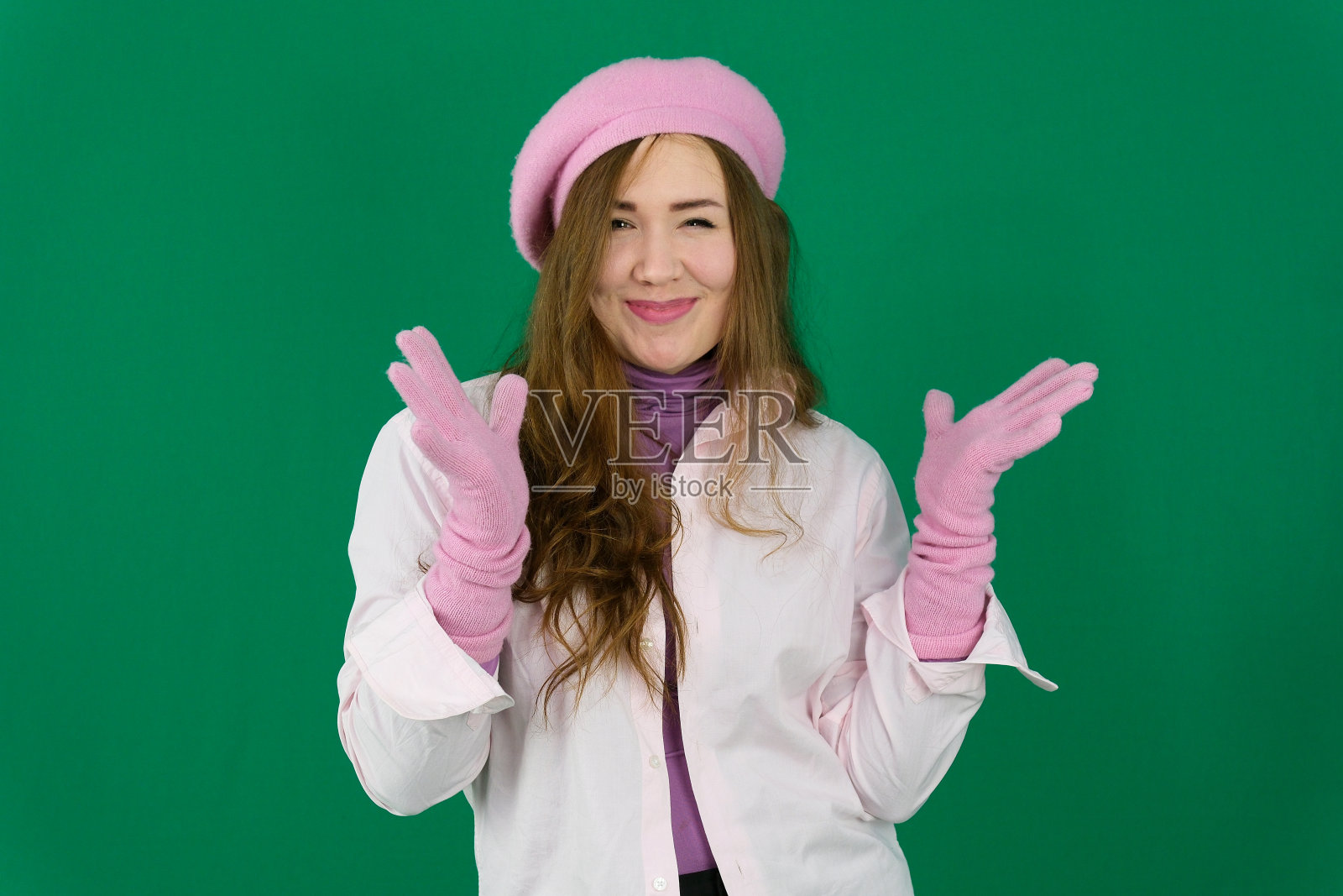 穿着粉红色制服的金发医生年轻女孩，头上戴着粉红色贝雷帽，绿色背景上的法国时尚。不同的情绪粉色夹克手套棕色长发。粉色秋冬针织手套戴在手上照片摄影图片