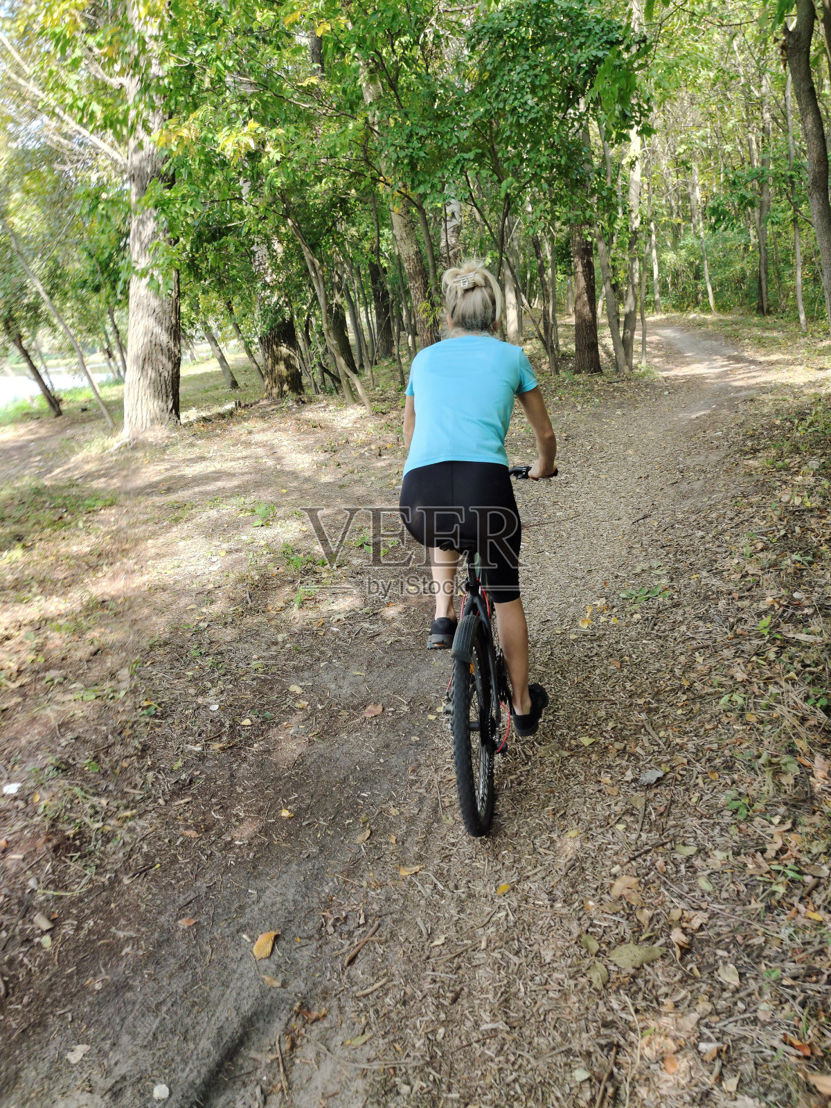 一位年轻女子在公园里骑自行车。在大自然中积极娱乐。后视照片摄影图片
