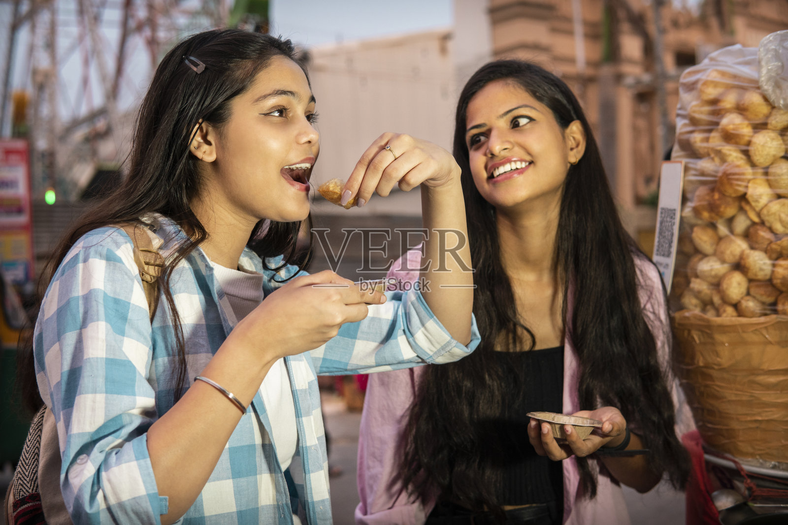 快乐的女性朋友在晚上一起享受街头小吃pani puri或golgappa。照片摄影图片