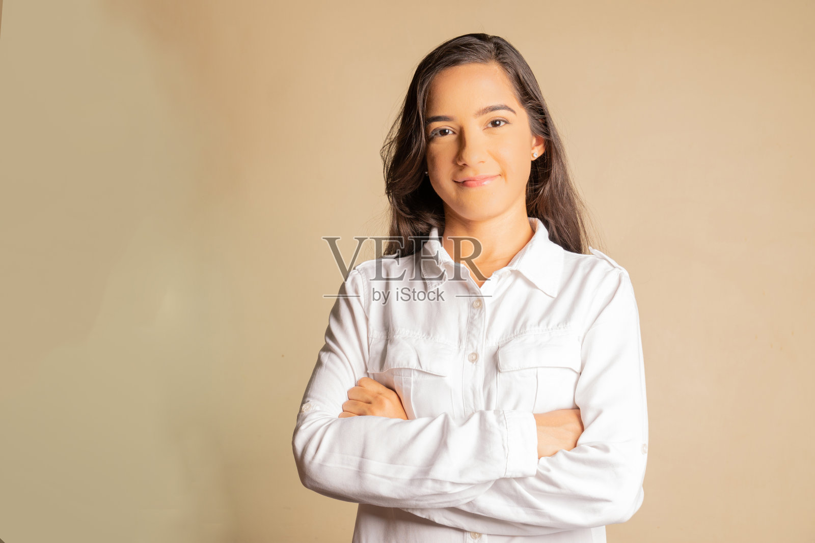 年轻的女商人面带微笑，双臂交叉，在一个中性的背景上期待着照片摄影图片