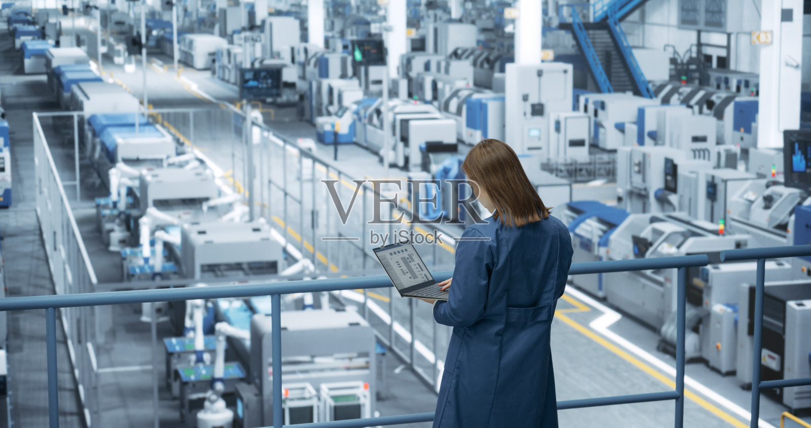亚洲女工程师站在工厂设施里，用笔记本电脑工作，研究和开发现代自动化机械臂生产电子产品的技术照片摄影图片