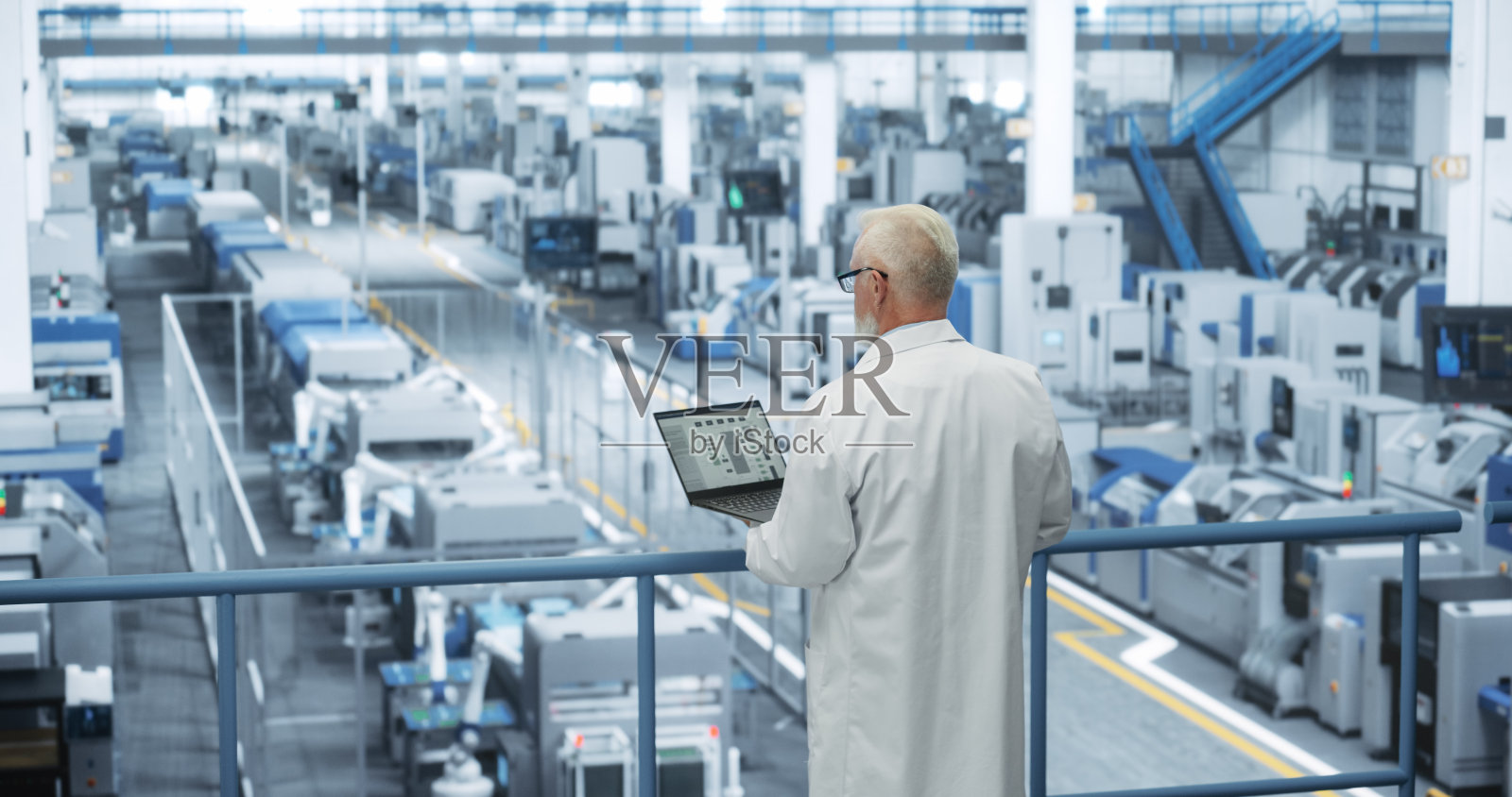 经验丰富的工业科学家穿着白大褂，使用笔记本电脑，俯瞰现代自动化电子制造与液压机械臂的生产照片摄影图片