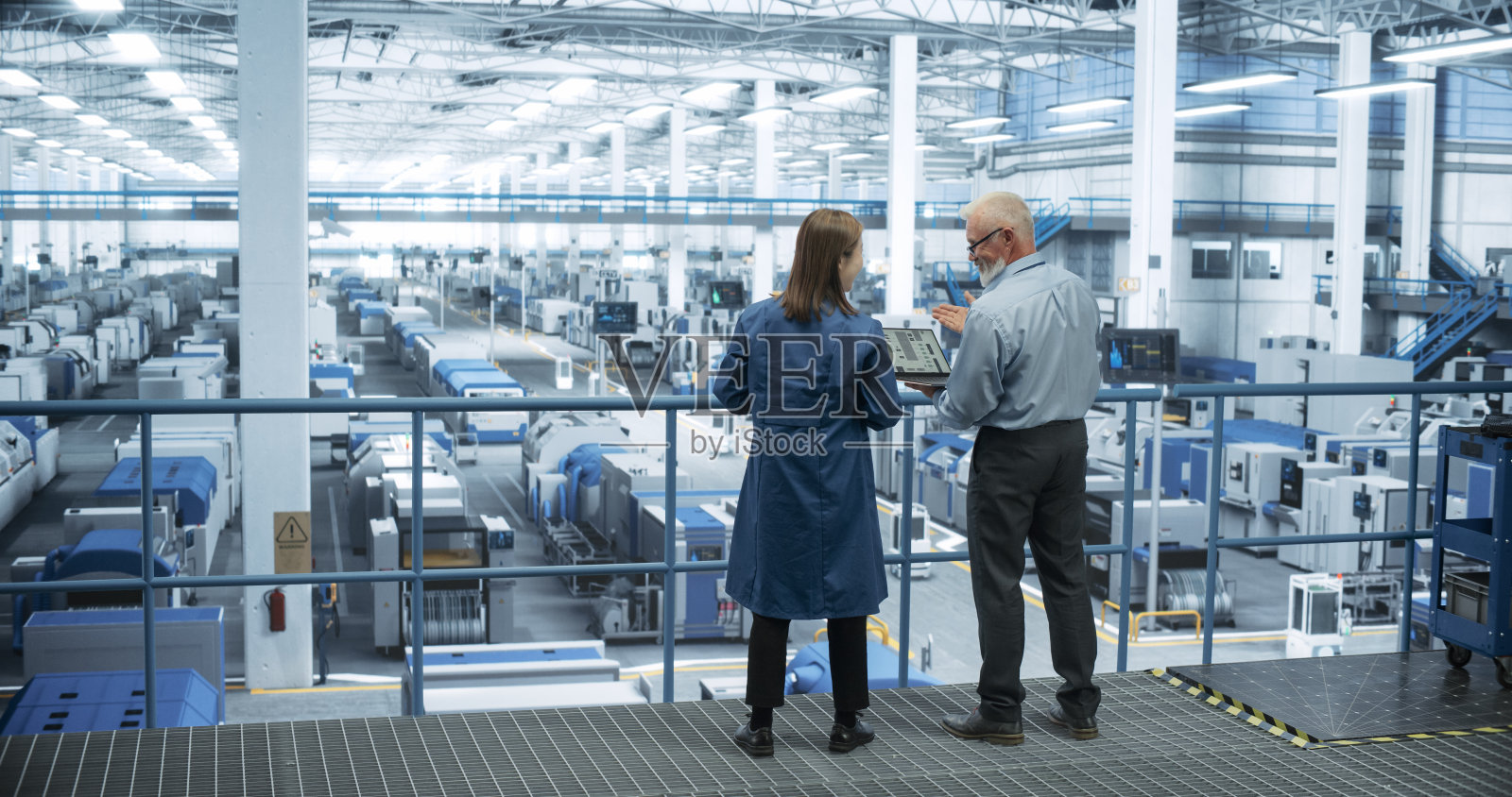 中年工程师和年轻的日本技术人员用笔记本电脑交谈。专家监控，分析软件报告在现代电子工厂照片摄影图片