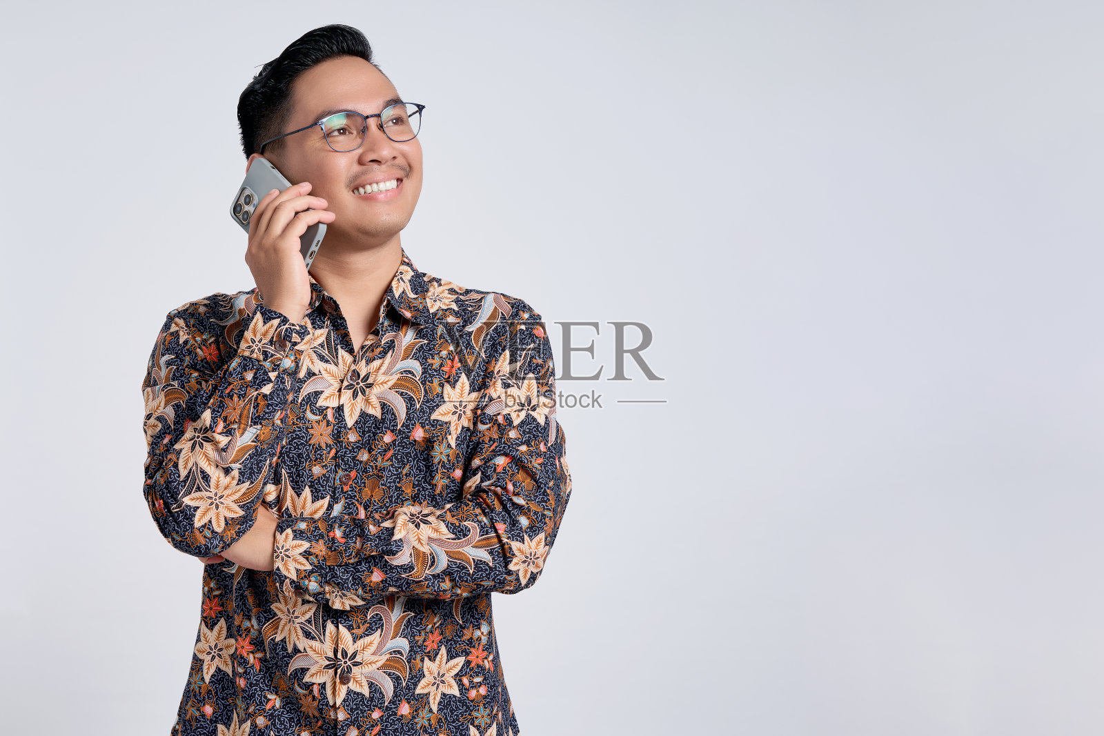 微笑快乐的亚洲年轻人穿着蜡染衬衫讲手机，看着复制空间孤立的灰色背景照片摄影图片
