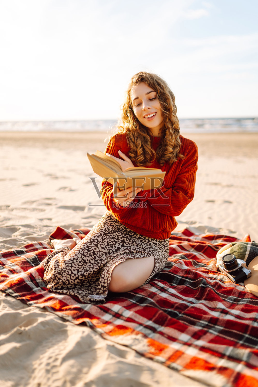 在海边的沙滩上野餐，年轻女子躺在毯子上看书。照片摄影图片