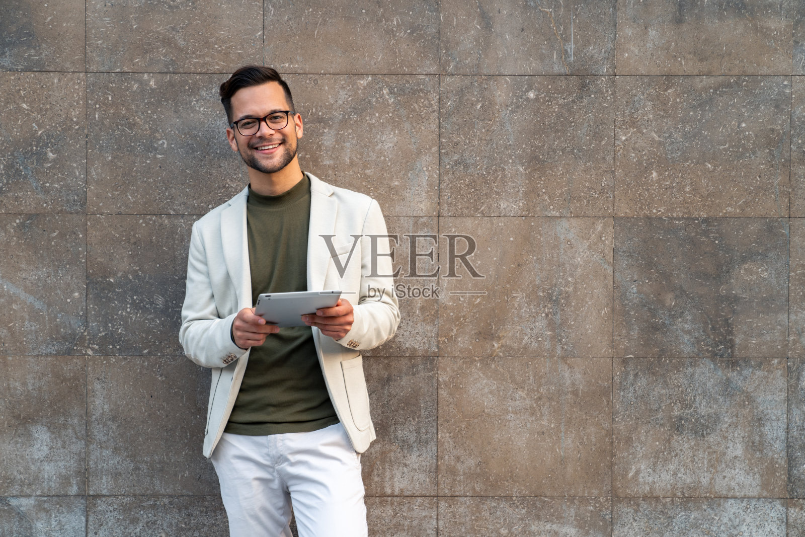 一个微笑的自信的商人，穿着西装，看着相机，用着数码平板电脑照片摄影图片