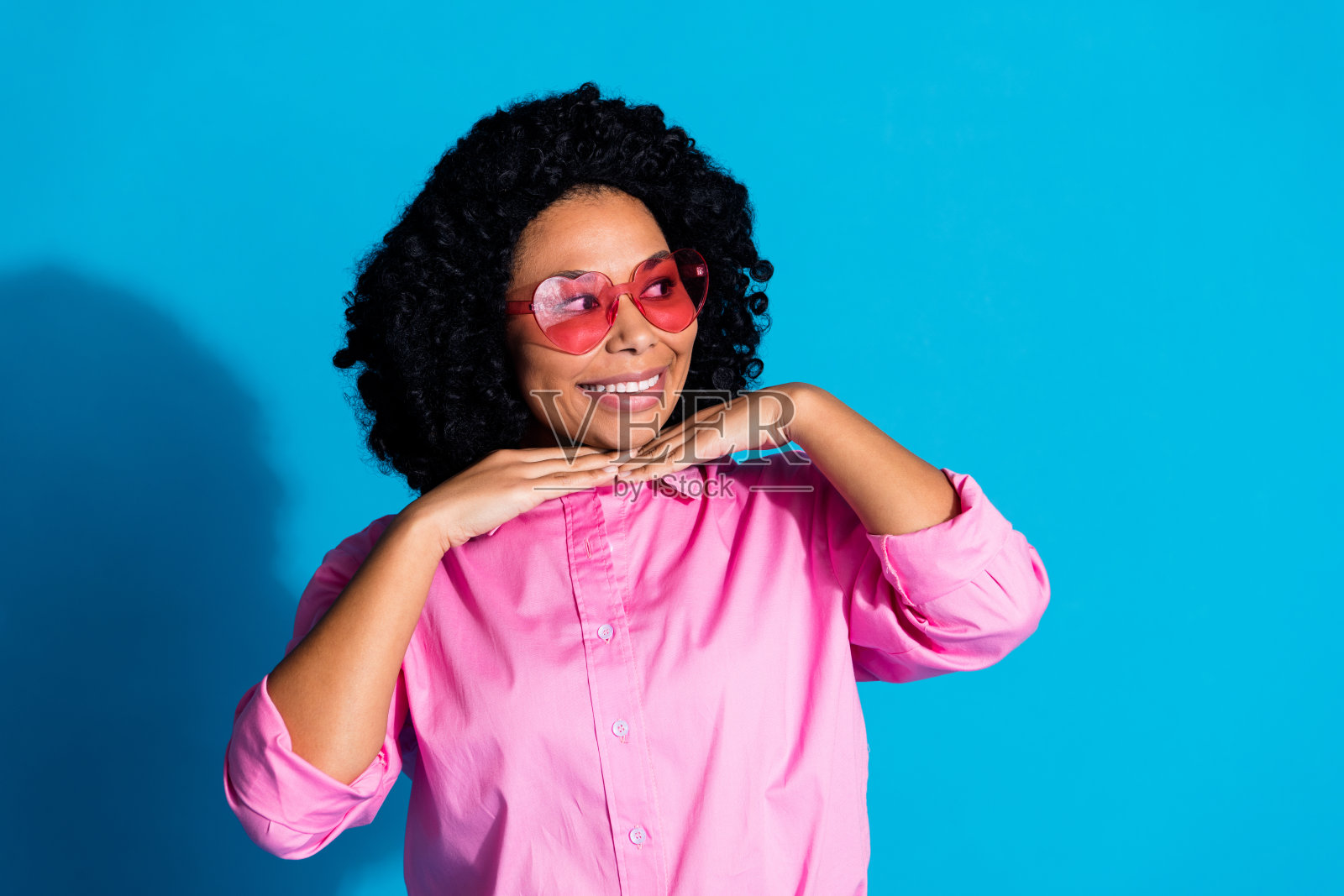 照片中漂亮的年轻女子笑容满面，看起来空无一人，穿着粉红色的衬衫，孤立在蓝色的背景上照片摄影图片