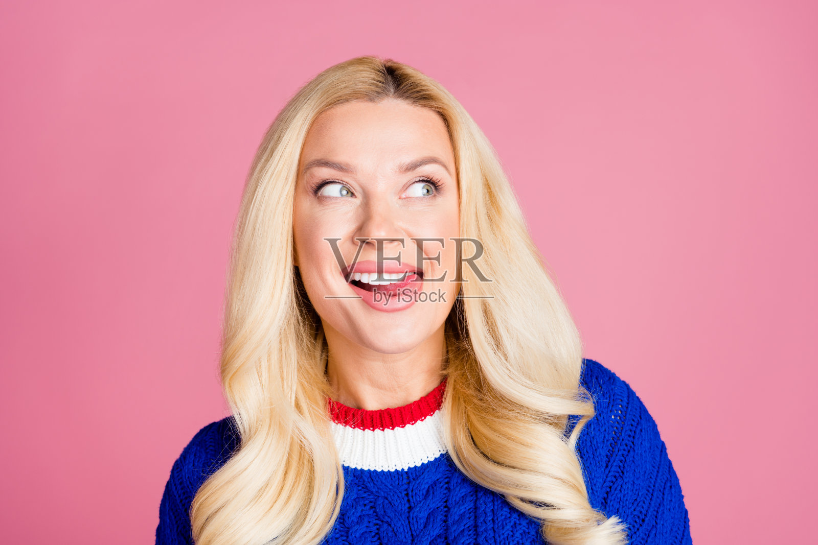照片的漂亮女士舌舔牙齿，看起来空白的空间，穿蓝色毛衣孤立在粉红色的背景照片摄影图片