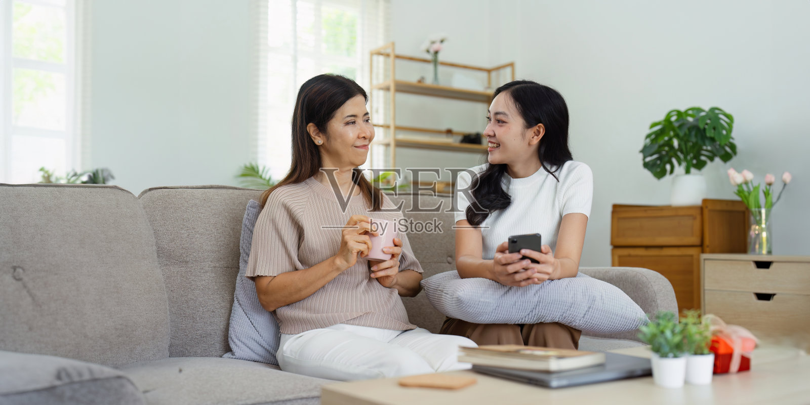 母亲和成年女儿一起坐在沙发上，母女俩周末一起聊天放松照片摄影图片