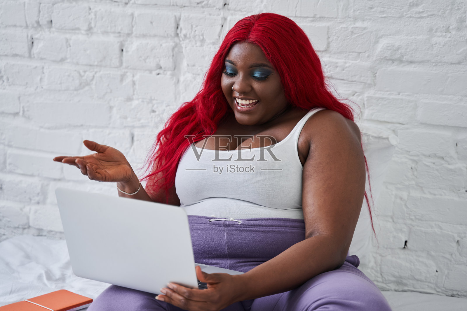 女人坐在床上，一边用笔记本电脑工作，一边用手势和视频通话聊天照片摄影图片