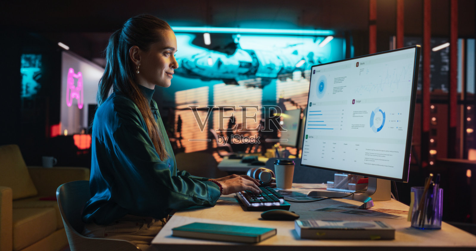 女性天才数字营销专家晚上在办公室用电脑工作。年轻的高加索女商人在创意机构，微笑和研究商业分析数据照片摄影图片