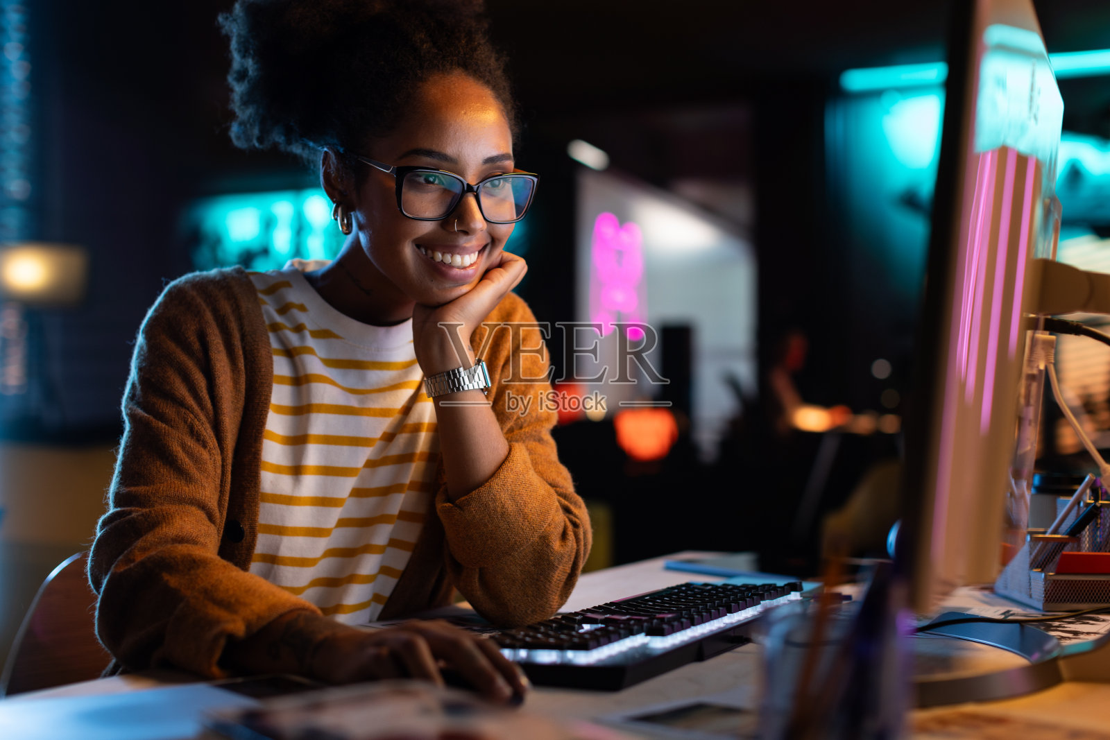 非裔美国女性在使用台式电脑检查数据和统计图表时微笑。一个快乐成功的黑人女商人在创意机构的肖像在晚上照片摄影图片