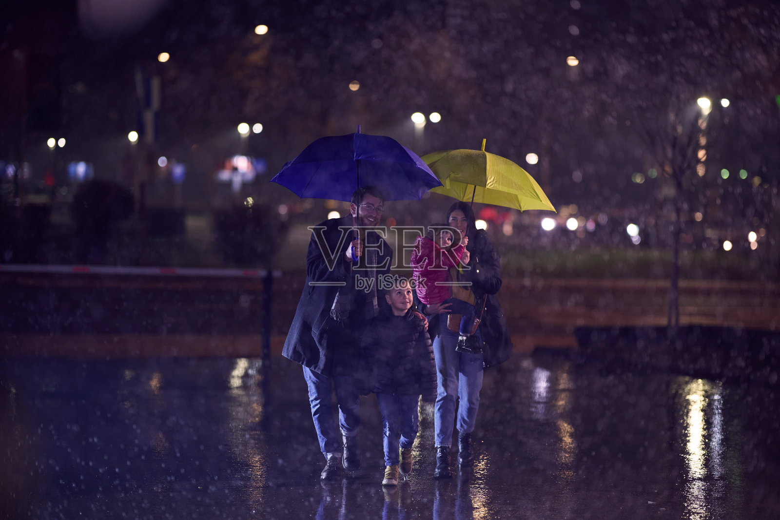 在一个下雨的城市夜晚，一对幸福的夫妇带着他们的孩子漫步在城市的街道上，走向电影院去看一场愉快的家庭电影照片摄影图片