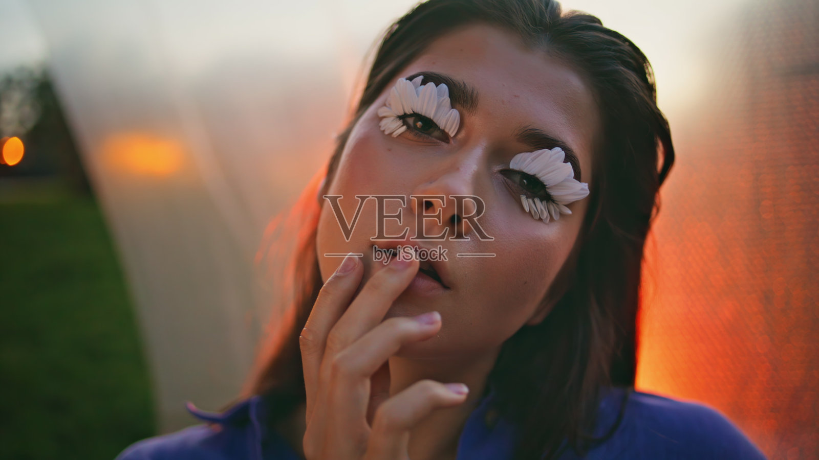 时尚模特在橙色灯光下触摸脸部特写，摆出花瓣状睫毛的姿势。照片摄影图片