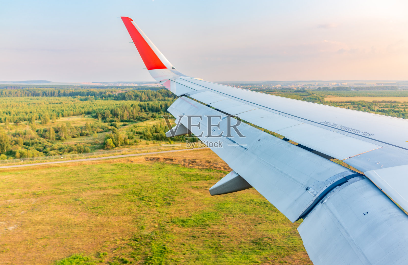 飞机机翼的视图，蓝天和绿色的土地在着陆。飞机窗口视图。照片摄影图片