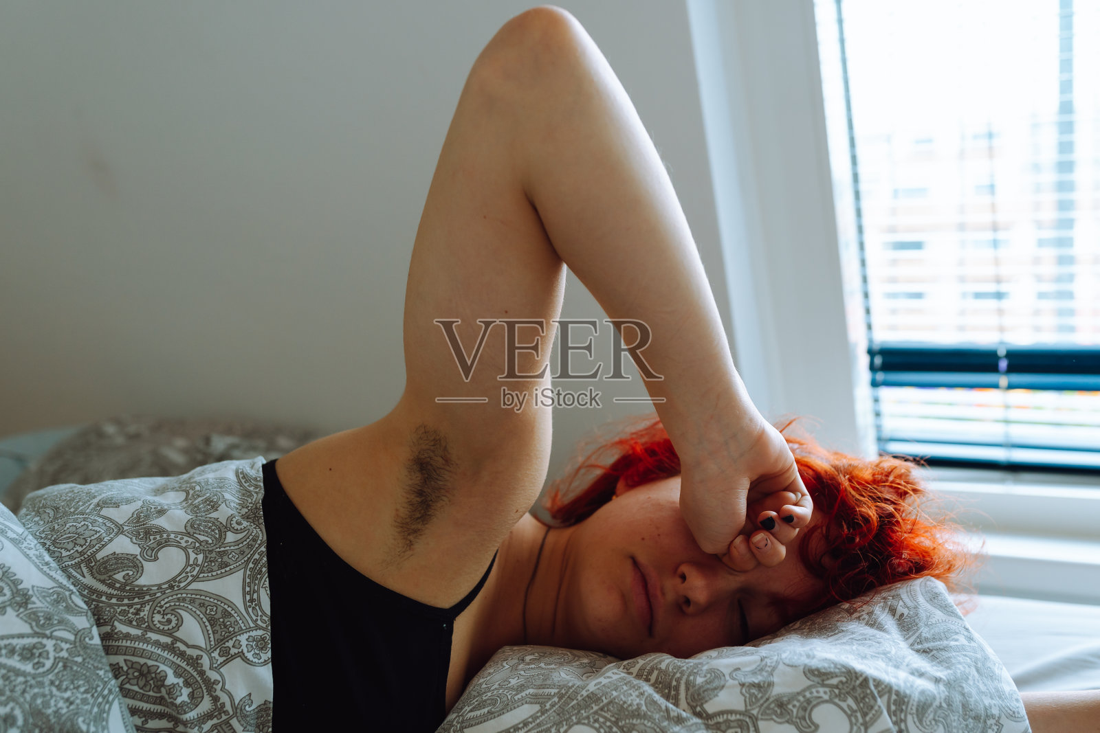 早上，年轻女子在床上醒来，腋下有自然的毛发照片摄影图片