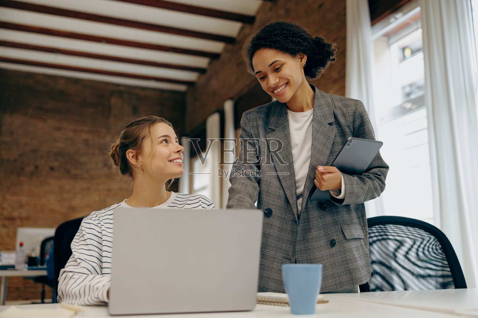 两个微笑的女同事坐在办公室里用笔记本电脑一起做项目照片摄影图片