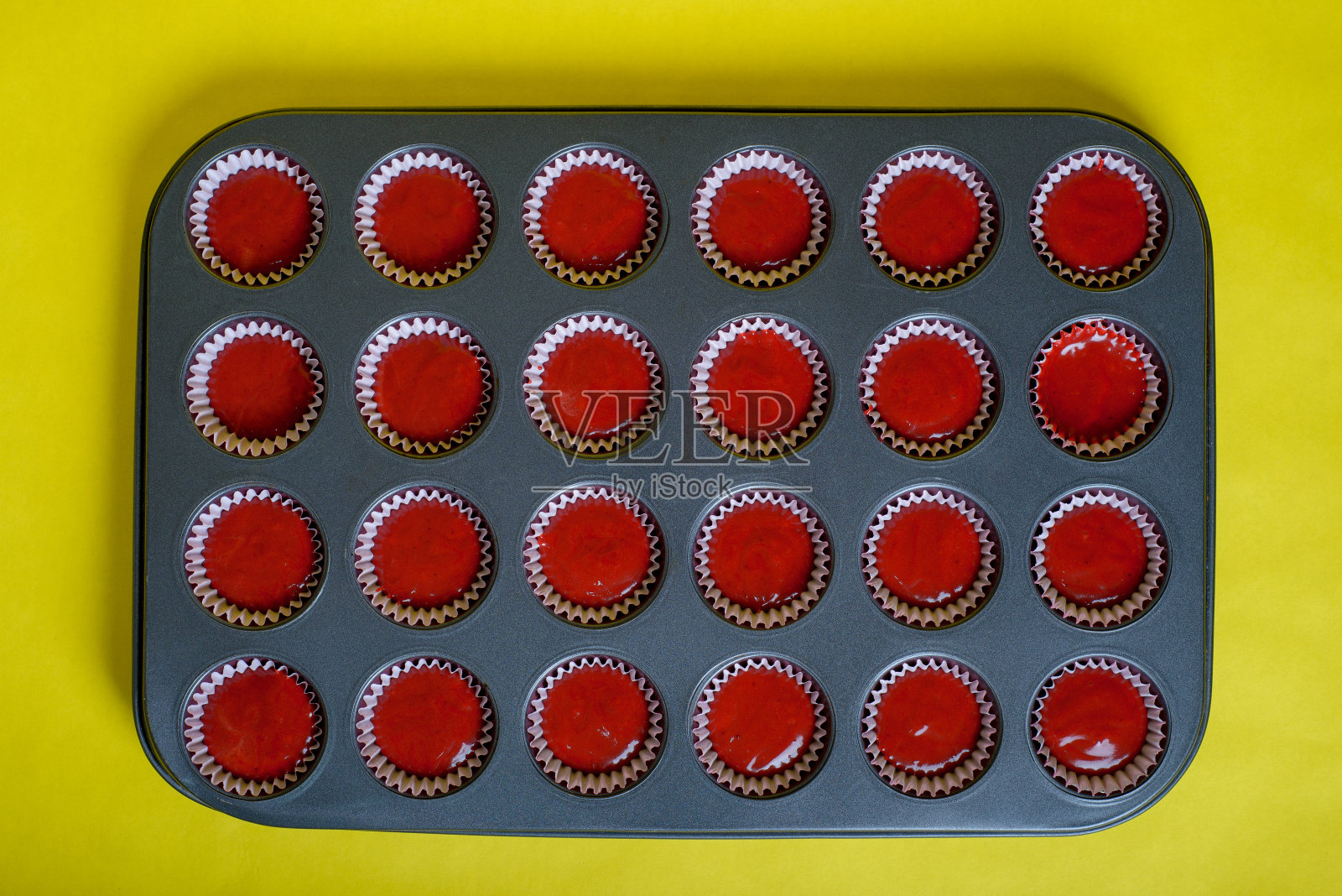托盘里放着混合好的红丝绒纸杯蛋糕原料，准备烘烤。黄色背景。照片摄影图片