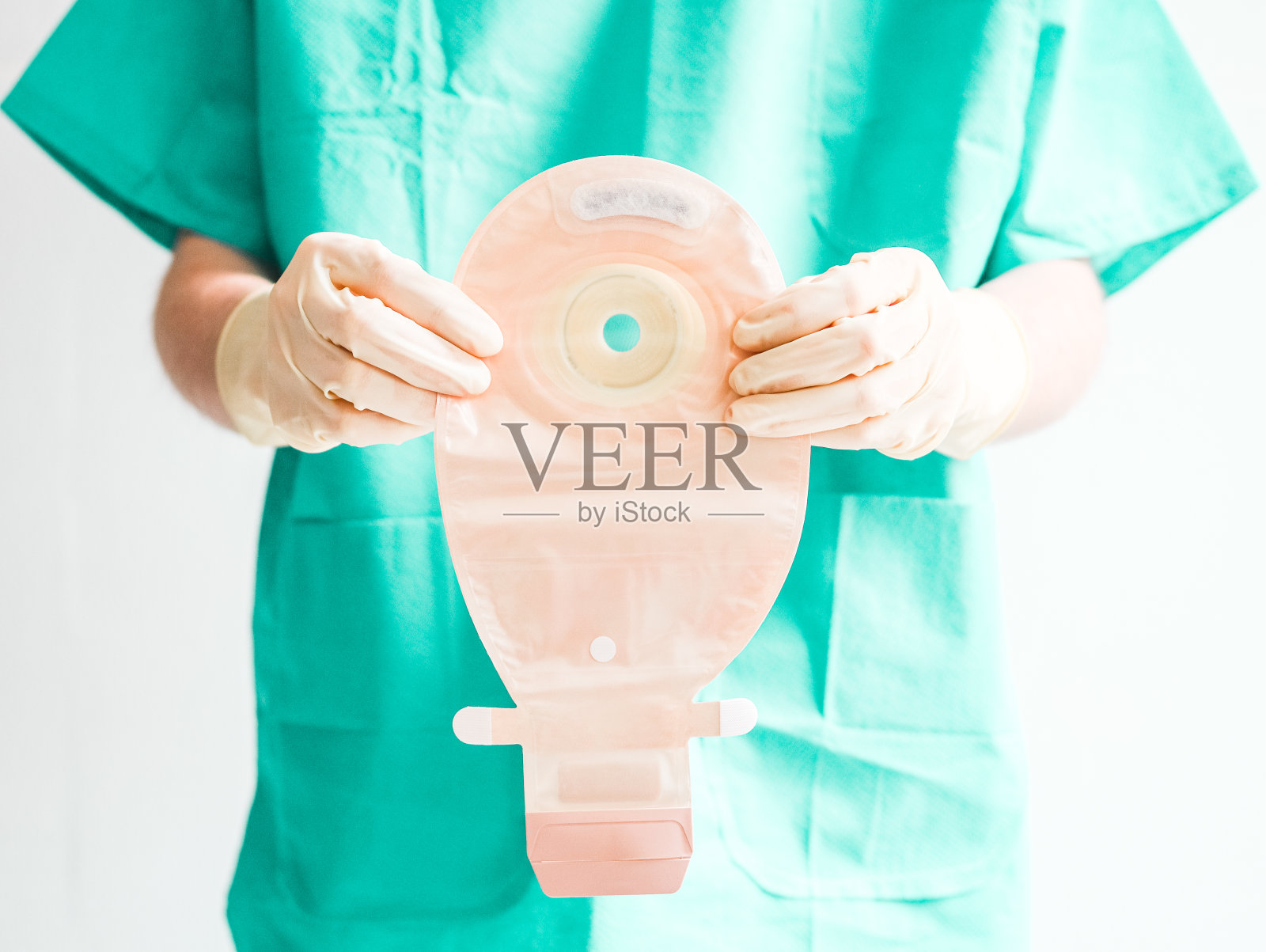 年轻的白人病人穿着绿色一次性医用睡衣，戴着无菌白手套，露出结肠造口袋照片摄影图片