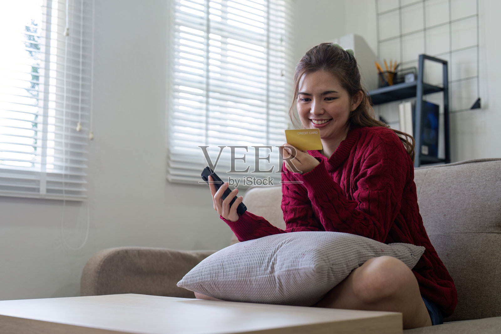 年轻的亚洲女性手持信用卡，使用智能手机进行网上购物。网上购物，在家网上支付照片摄影图片