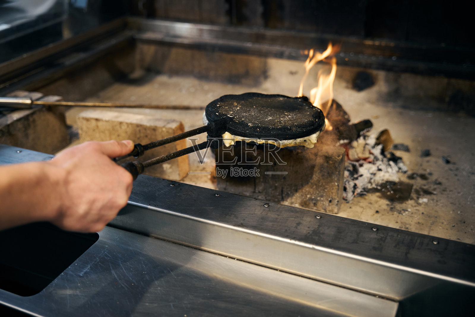 矮个男厨师在烧饼机里用手在燃烧的火堆里煎煎饼照片摄影图片