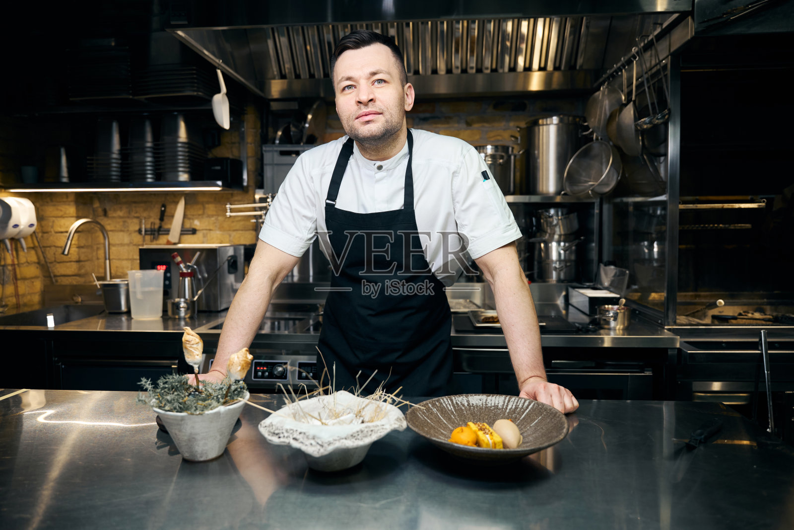 餐馆里，白人男厨师端着三道菜站在桌前照片摄影图片