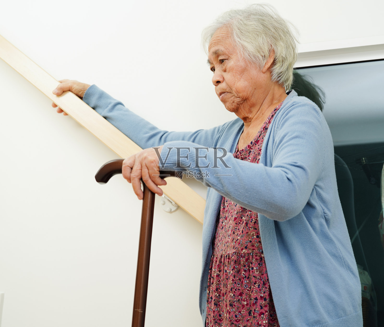亚洲老年妇女在护理人员的帮助下使用拐杖下楼梯，防止意外，滑倒和跌倒。照片摄影图片