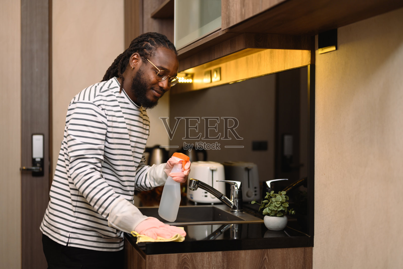 戴着防护手套的千禧一代男子用清洁喷雾和布清洁厨房柜台照片摄影图片