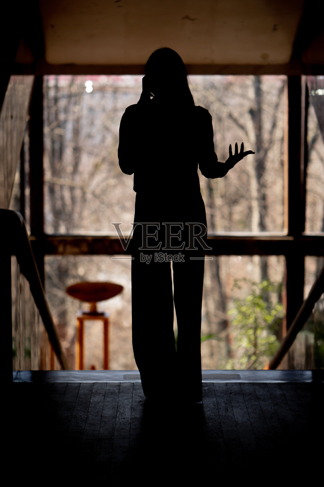 在办公室的平台上，在背光下俯瞰窗户，女孩正在打电话照片摄影图片