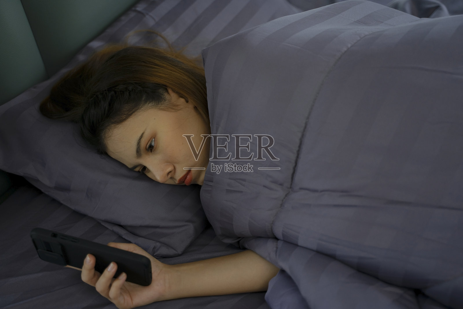 漂亮女人醒来后玩她的智能手机。照片摄影图片