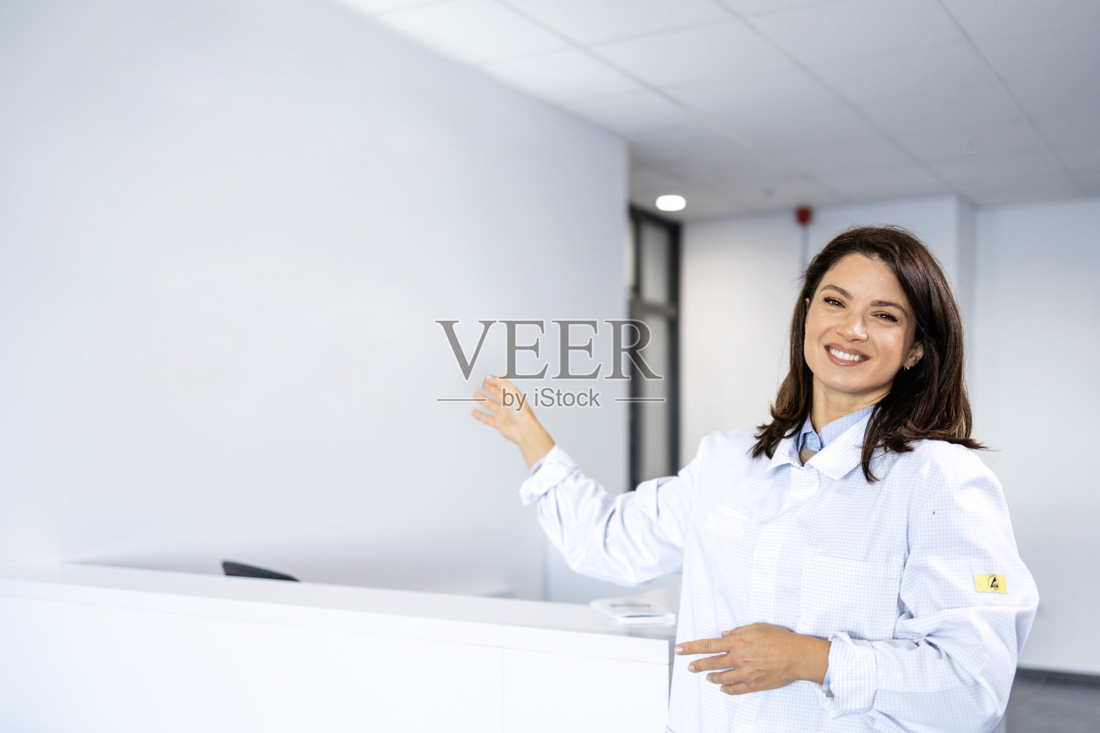 微笑的美丽女医生站在医院大厅欢迎新病人的画像。照片摄影图片