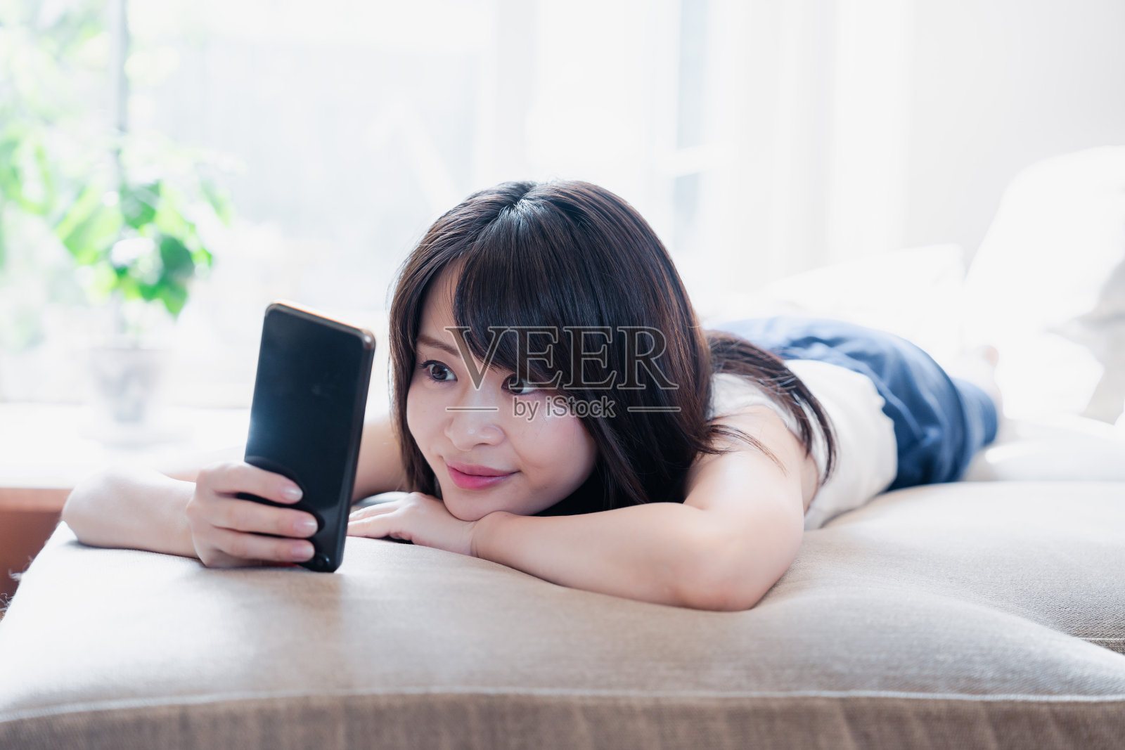 年轻女子躺在沙发上玩智能手机照片摄影图片