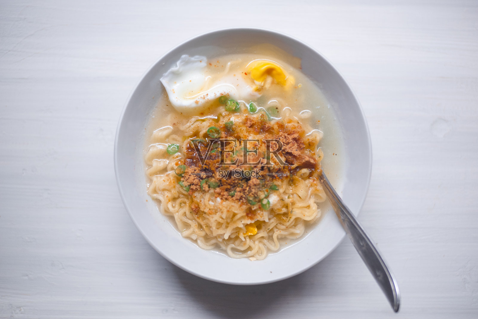 煮过的方便面，上面有鸡蛋和辣椒片，放在白色的碗里，白色的背景分开。照片摄影图片